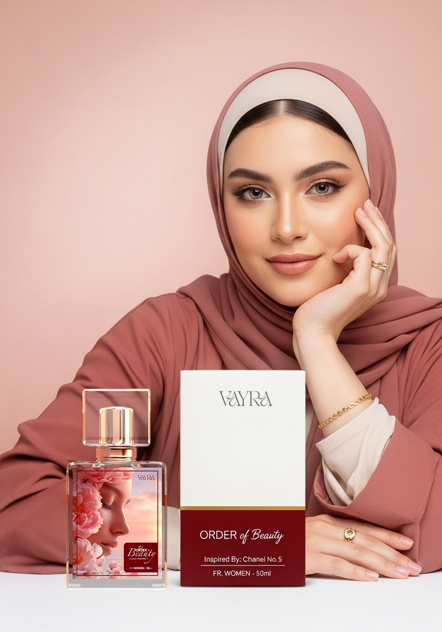 Alt Text: Elegant studio shot of a model in a pink hijab resting her face on her hand next to a bottle and box of Vayra Order of Beauty perfume. 50ml fragrance for women inspired by Chanel No. 5 with floral label design.