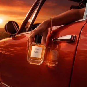 A hand holding Vayra Dunhill Desire bottle out of a red vintage car window; best fragrance in Pakistan.